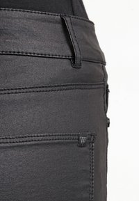 Jeans de denim negro con una textura suave, con costuras en contraste, una pequeña etiqueta de la marca en el bolsillo trasero y un diseño ajustado.