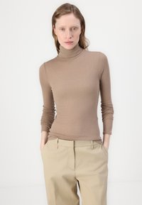 Brun ribbestrikket turtleneck-genser med lange ermer, kombinert med lysebeige bukser, som har en glatt tekstur og en tettsittende design.