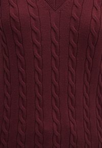 Burgunderfarbener Strickpullover mit V-Ausschnitt und strukturierten Kabelmustern im gesamten Stoff, die eine gerippte Optik mit glatter Textur erzeugen.
