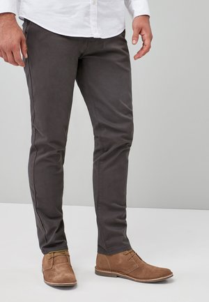 Pantalones de algodón grises con un corte ajustado, que presentan costuras prominentes y una textura suave, combinados con botas de ante marrón claro con cordones.