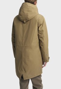 Hnedá nepremokavá parka s veľkou kapucňou, prešívanou podšívkou, bočnými vreckami a cvokovým zapínaním na leme. Obsahuje logo na rukávoch.