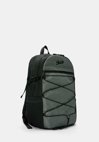 Sac à dos noir et gris avec un motif en hexagone à l'avant, un laçage à cordon élastique, une poche avant zippée, une sangle latérale ajustable et une poignée supérieure.