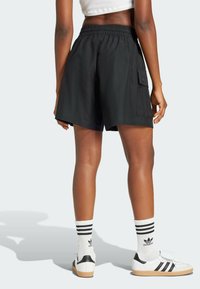 Pantalones cortos cargo negros con cintura elástica y bolsillo lateral, hechos de tela suave. Combinados con zapatillas blancas y calcetines a rayas.