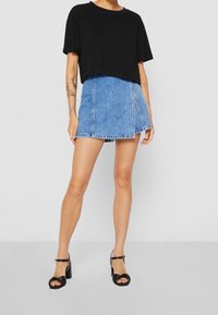 Svart cropped t-shirt, blå denim miniskirt med sömdetalj fram, och svarta klacksandaler med tvinnade remmar.
