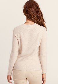 Pull beige clair en tissu doux, avec un tricot texturé, des manches longues et un ourlet côtelé avec de subtils accents chinés.