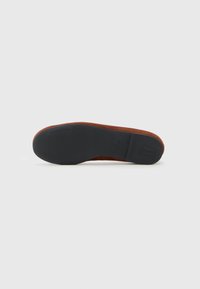 Chaussure en daim marron avec une semelle en caoutchouc noir lisse. La chaussure présente un bout arrondi et un design minimaliste, mettant en valeur des lignes épurées.