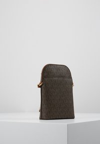 Brun mönstrad väska med rundad topp, guldfärgad dragkedja och dragkedjestängning. Materialet har en texturerad yta och subtila varumärkesdetaljer.