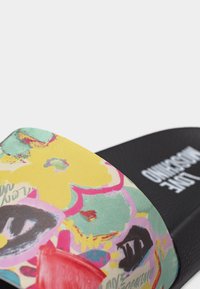 Πολύχρωμο σανδάλι slide με λουλούδια και φαρδιά λουρί, μαύρη σόλα με λευκό λογότυπο της μάρκας.