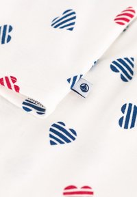 Tissu en coton avec un fond blanc présentant des cœurs rouges et bleu marine. Les cœurs présentent des motifs variés, comprenant des motifs unis et rayés. Étiquette de logo incluse.