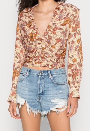 Kvinde iført flæset, blomsterprintet crop top med lange ærmer i orange toner, kombineret med højtaljede, distressed lyse denimshorts.