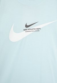 Šviesiai mėlynas medvilninis marškinėlis su ryškiu juodai baltu Nike swoosh logotipu ir tekstu „Nike Athletic Dept.“. Minkšta tekstūra, apvalus kaklas.