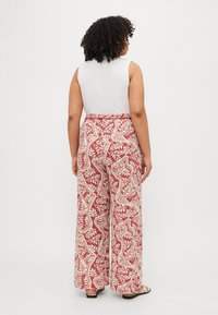 Pantaloni evazați cu un model floral roșu și crem, având talie înaltă și un material moale, ușor. Textură netedă, design casual.
