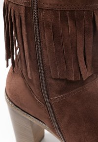 Stivaletto alla caviglia in camoscio marrone con cerniera laterale, decorato con lunghe frange e tacco spesso, che presenta una texture liscia e cuciture dettagliate.