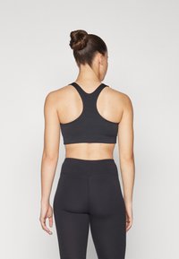 Sujetador deportivo negro con un diseño de espalda nadadora, hecho de material elástico. Combinado con mallas negras de cintura alta. Textura suave, costuras mínimas.