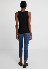 Svart ärmlös topp i mjukt tyg, kombinerad med slim-fit blå jeans. Outfiten komplett med svarta skor. Bakifrån visad.