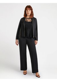 Giacca nera con zip e inserti in pizzo, pantaloni a gamba larga, tutto in tessuto nero, con una texture liscia e lucida e minimi dettagli decorativi.