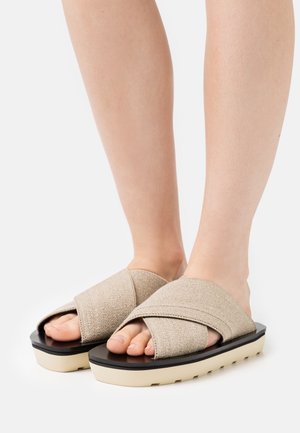 Beige stofskridtsandaler med krydsremdesign, med en sort platformsål og cremefarvet bund. Glat tekstur, åben-tå stil.