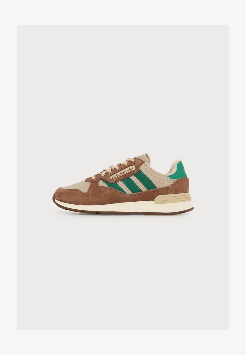 Baskets Adidas beige et marron avec des bandes vertes, semelle beige et détail vert au talon, montrées de côté sur un fond neutre.