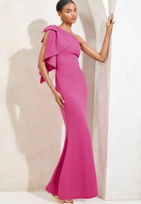 Fuksia yhdelle olalle suunniteltu mekko, jossa on röyhelöhiha, istuva vartalo ja liehuva helma. Valmistettu sileästä kankaasta, joka korostaa eleganttia siluettia.