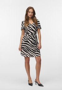 Kvinde står iført en knælængde kjole med sort-hvidt zebra-print, korte ærmer og sorte slingback-sko med hæl.