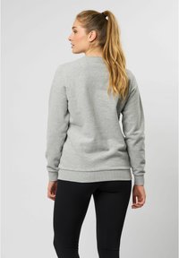 Grijze katoenen sweatshirt met ronde hals en ribbelmanchetten, van de achterkant bekeken, gecombineerd met zwarte leggings. Soepele textuur, minimalistisch ontwerp.