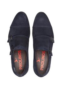 Zapatos de ante azul marino con dos hebillas, puntera redondeada y costuras en contraste. El interior presenta un estampado de logo rojo sobre un cojín oscuro.