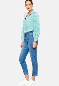 Turkoosi raidallinen paita, jossa on ilmapallo-hihat ja nappilista; yhdistetty kapeisiin sinisiin farkkuihin ja valkoisiin lenkkareihin.