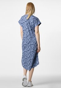 Sininen kukallinen mekko, jossa on lyhyet hihat ja rento malli, valmistettu kevyestä kankaasta, polvimittainen helma ja sivuaukot, yhdistettynä valkoisiin lenkkareihin.