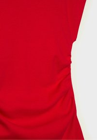 Vêtement rouge à manches courtes avec un détail de tissu froncé du côté droit, sur un fond clair uni.