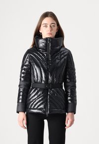 Giacca a vento nera con colletto alto, texture lucida, design imbottito e vita con cintura. Presenta cuciture diagonali e una zip frontale.