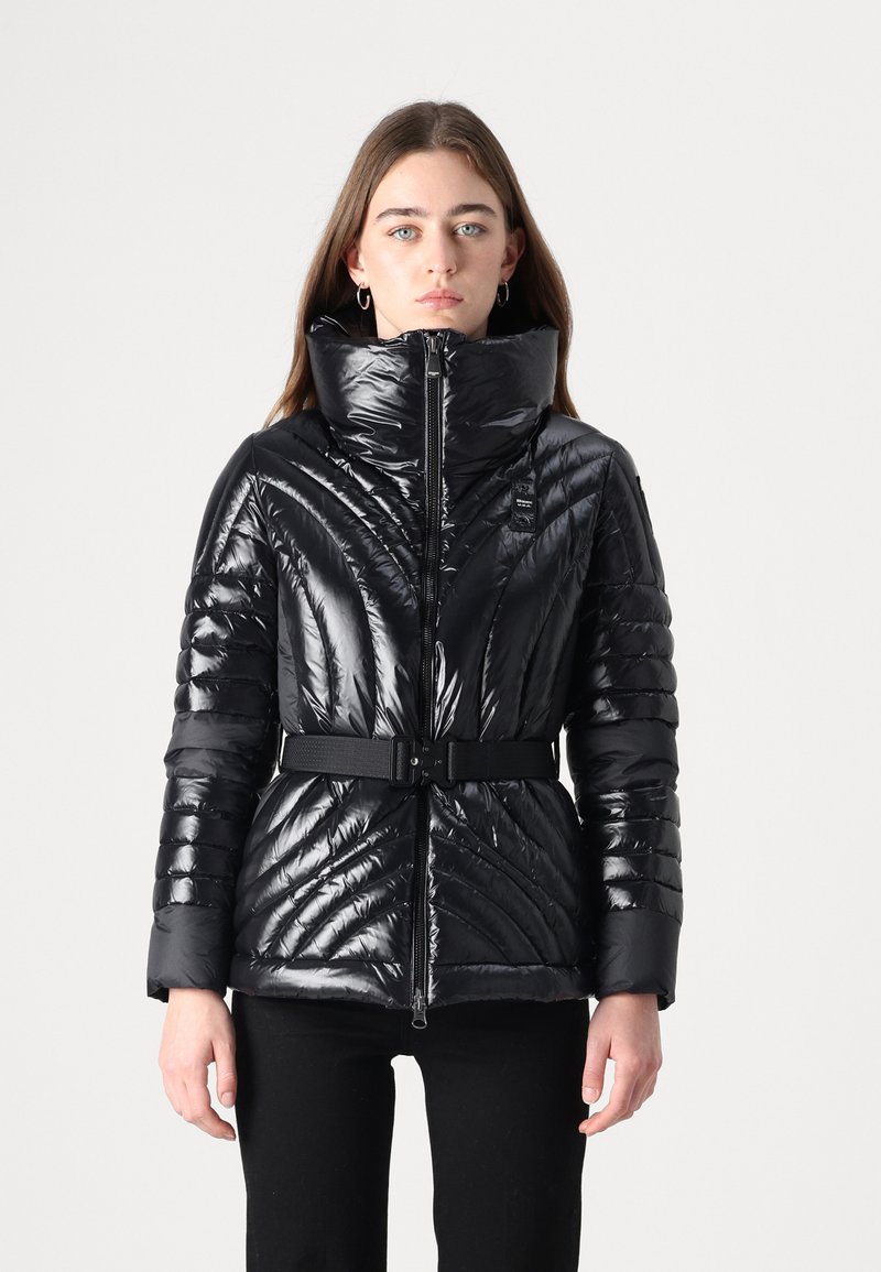 Giacca a vento nera con colletto alto, texture lucida, design imbottito e vita con cintura. Presenta cuciture diagonali e una zip frontale.