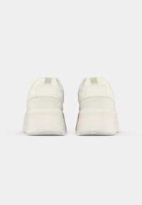 Białe sportowe sneakersy o teksturowanym wykończeniu, z grubą gumową podeszwą i minimalistycznym designem. Niski profil z miękkim akcentującym uchwytem.