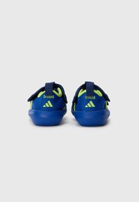 Blue athletic shoes with a mesh upper, green accents, and Velcro straps. Rounded toe and textured rubber sole for grip.