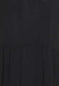 Vestido negro con una textura suave, que presenta una cintura fruncida y un sutil volante. Incluye un detalle de cordón en el escote.