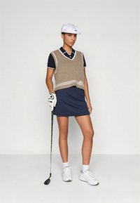 Strój golfowy z brązową dzianinową kamizelką na granatowej koszulce polo, zestawiony z prążkowaną granatową spódnicą. Do tego biała czapka, białe trampki i rękawica do golfa.