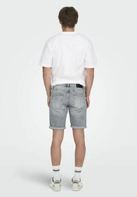 Camiseta blanca de manga corta, pantalones cortos de mezclilla gris claro con dobladillos enrollados, y calcetines blancos con rayas de colores, combinados con calzado casual.