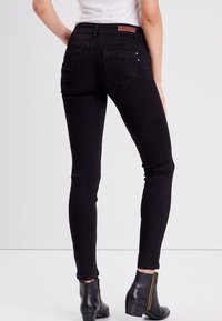 Mustat skinny-farkut, joissa on korkea vyötärö, kapea istuvuus ja takataskut. Yhdistettynä nilkkasukkiin.