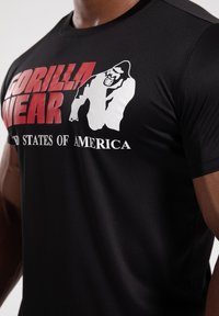 Black athletic t-shirt featuring bold "GORILLA WEAR" text in red and white, with a gorilla graphic. Made of smooth, lightweight fabric.