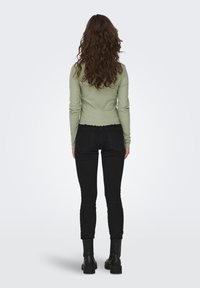 Långärmad, ribbad, ljusgrön topp med vågig nederkant, tillsammans med figurnära svarta jeans och svarta ankelstövlar.