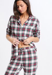 Ensemble de pyjama en flanelle à carreaux rouges, verts et blancs, comprenant une chemise à boutons avec une poche poitrine et un pantalon à cordon. Tissu texturé.