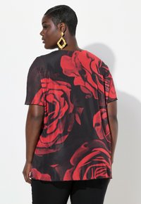 Top nero con grandi stampe di rose rosse, maniche corte e una vestibilità rilassata. Il tessuto appare leggero e liscio, con un orlo curvo.