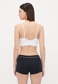 Bralette branca com alças finas e uma textura suave, combinada com calções pretos com um detalhe branco na cintura.