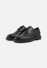 Chaussures en cuir noir avec une finition lisse, bout rond et design à lacets. Semelle en caoutchouc robuste avec des accents de couture discrets.