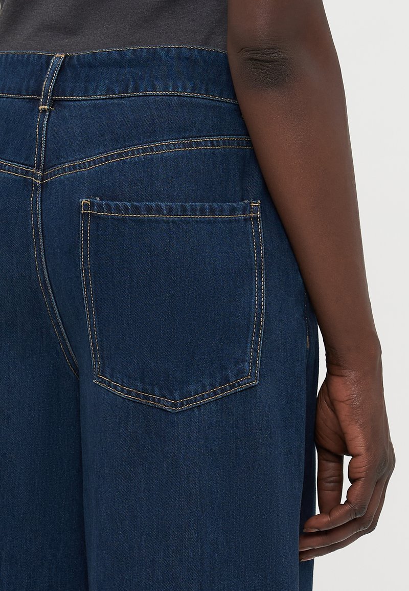 Ciemnoniebieskie dżinsy o prostym kroju, z tylną kieszenią z kontrastowym przeszyciem oraz gładką, teksturowaną powierzchnią.