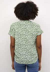 Short-sleeve blouse in a lightweight, textured fabric. Design features a green animal print on a white background. Hemline is slightly longer at the back.