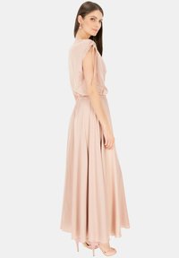 Długa sukienka w kolorze różowym z marszczoną talią, zwiewnym dołem, krótkimi rękawami i wiązaniami na ramionach. Modelka w dopasowanych różowych szpilkach. Gładka tekstura.