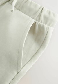 Světlé zelené bavlněné tepláky s měkkou texturou, s elastickým pasem a detailem boční kapsy. Součástí je také odpovídající šňůrka na stažení.