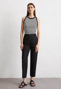 Zwart-wit gestreepte tanktop gecombineerd met op maat gemaakte zwarte broeken. Het model draagt vlakke zwarte sandalen met een gouden gespaccent.