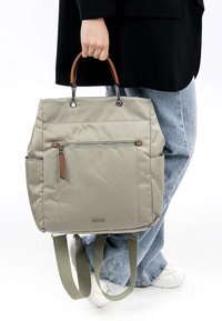 Beige Nylon-Rucksack mit braunen Ledergriffen, einer vorderen Reißverschlusstasche, zwei seitlichen Taschen und verstellbaren grünen Trageriemen.