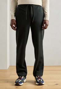 Pantalons de survêtement gris foncé avec un waistband à cordon de serrage, coupe droite et texture douce, associés à des baskets colorées.